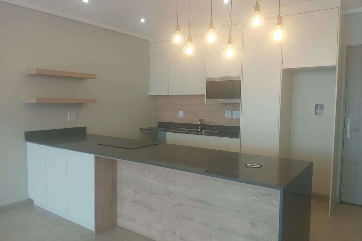 Modern kitchen featuring sleek white and wood-tone cabinetry, stone countertops, a central island, integrated microwave, and stylish pendant lighting in an open-plan layout.