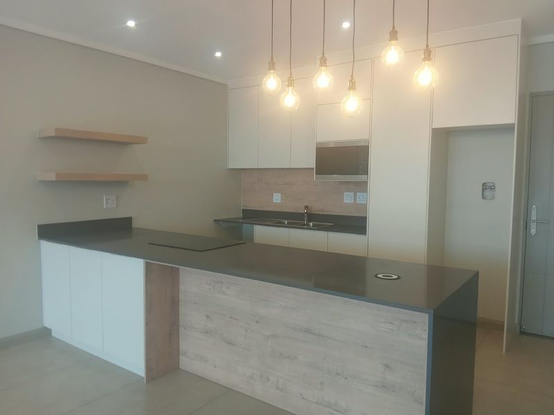 Modern kitchen featuring sleek white and wood-tone cabinetry, stone countertops, a central island, integrated microwave, and stylish pendant lighting in an open-plan layout.