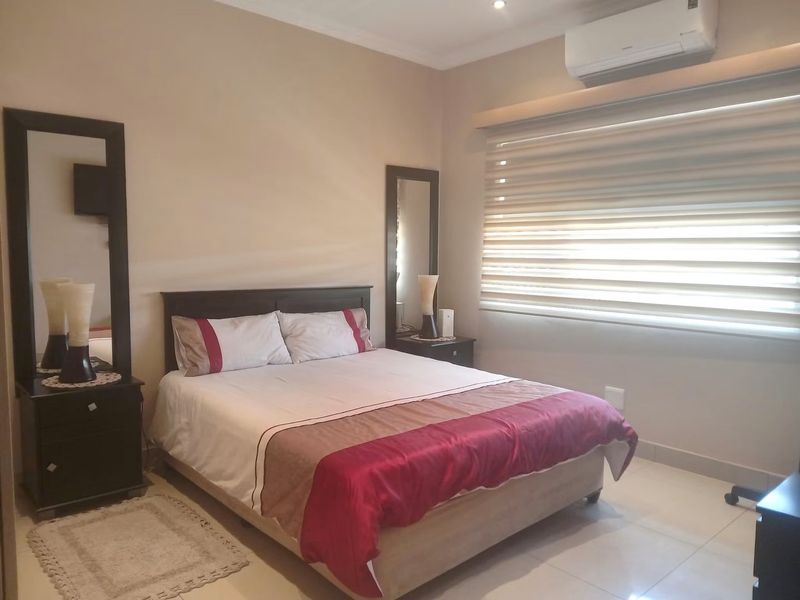 A well-maintained bedroom featuring tiled flooring, a wall-mounted split-system air conditioner, and modern roller blinds for light control.