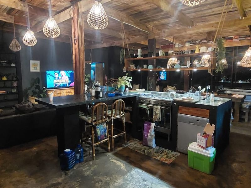 Spacious open-plan living and kitchen area featuring exposed timber ceiling beams, a central kitchen island with built-in stove, and polished concrete flooring.