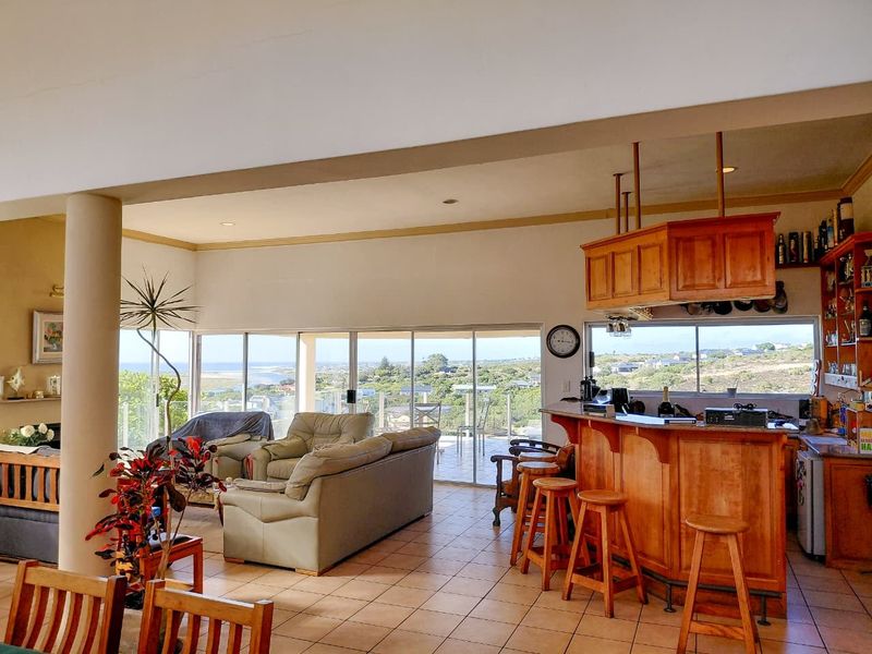 Spacious open-plan living area featuring a built-in wooden bar, tiled flooring, and large sliding glass doors offering expansive coastal and landscape views.