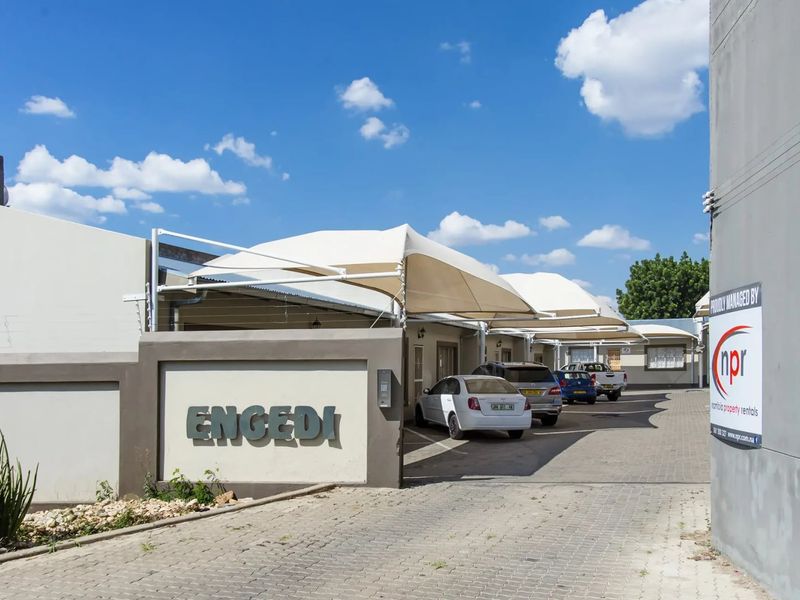 Front entrance view of the townhouse complex featuring a paved driveway, dedicated shade sail parking bays, and clear property signage.
