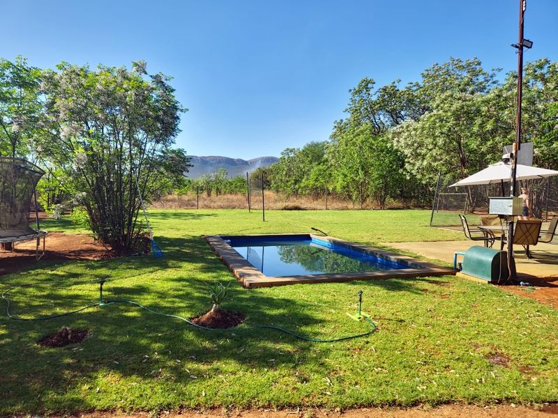A well-maintained outdoor pool area featuring a rectangular swimming pool with wooden decking, set within a spacious garden with mountain views.