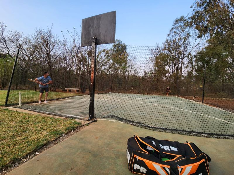 Outdoor sports facility featuring a hardcourt surface with perimeter netting and a basketball backboard, suitable for recreational activities.