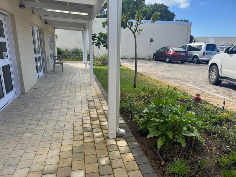A clean, covered paved patio area adjacent to a landscaped garden bed and parking area in a retirement village setting.