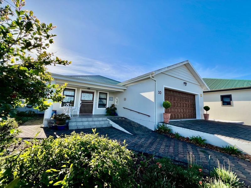 Front elevation of a well-maintained house featuring a paved driveway, double garage, and a welcoming entrance with tiled steps and a security gate.