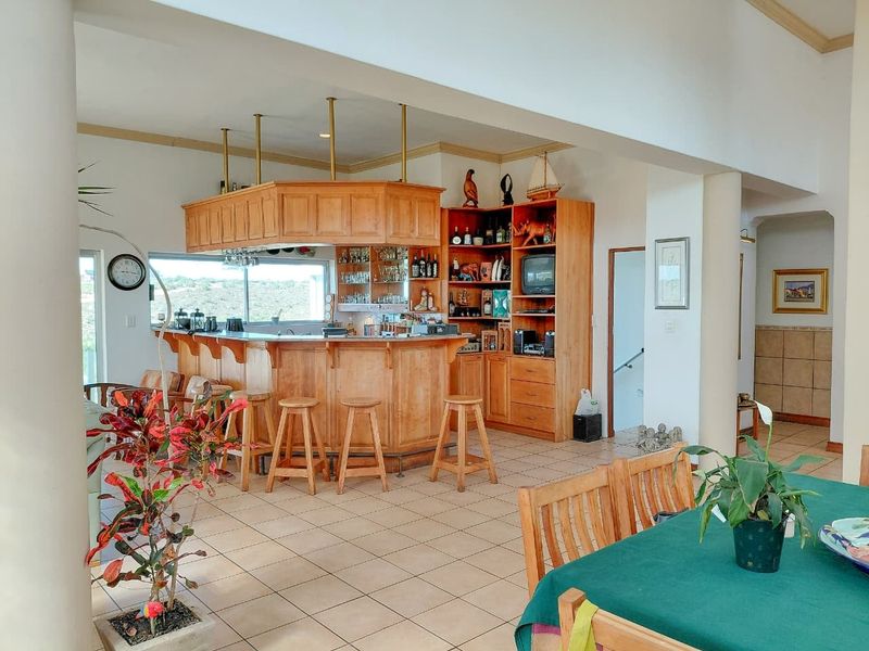 A spacious open-plan area featuring a large built-in wooden bar with integrated cabinetry and shelving, set against a tiled floor and neutral walls.