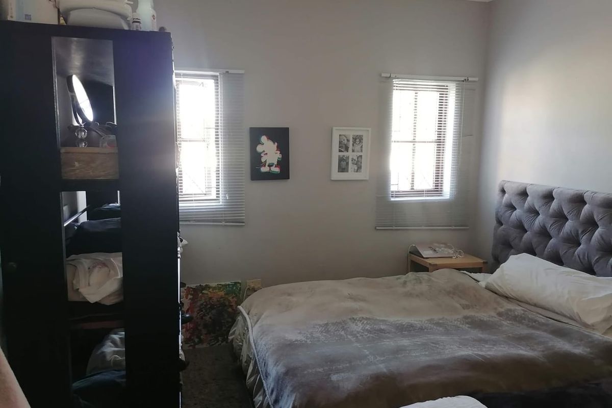 A bedroom featuring two windows with venetian blinds and a tufted upholstered headboard.