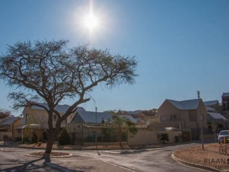 A clear street view of the residential neighborhood approach, featuring paved roads, street lighting, and established trees under a bright sky.