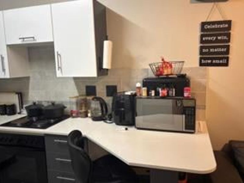 A compact kitchen featuring modern white and grey cabinetry, a built-in electric hob and oven, and a functional laminate countertop with tiled backsplash.