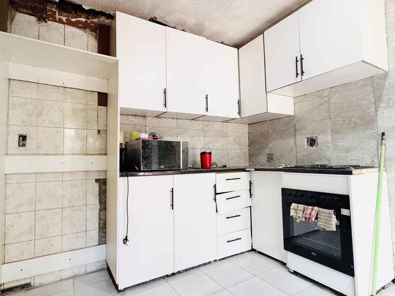 A kitchen in need of renovation, featuring built-in cabinetry, a built-in oven, and tiled surfaces with visible structural and finish damage.