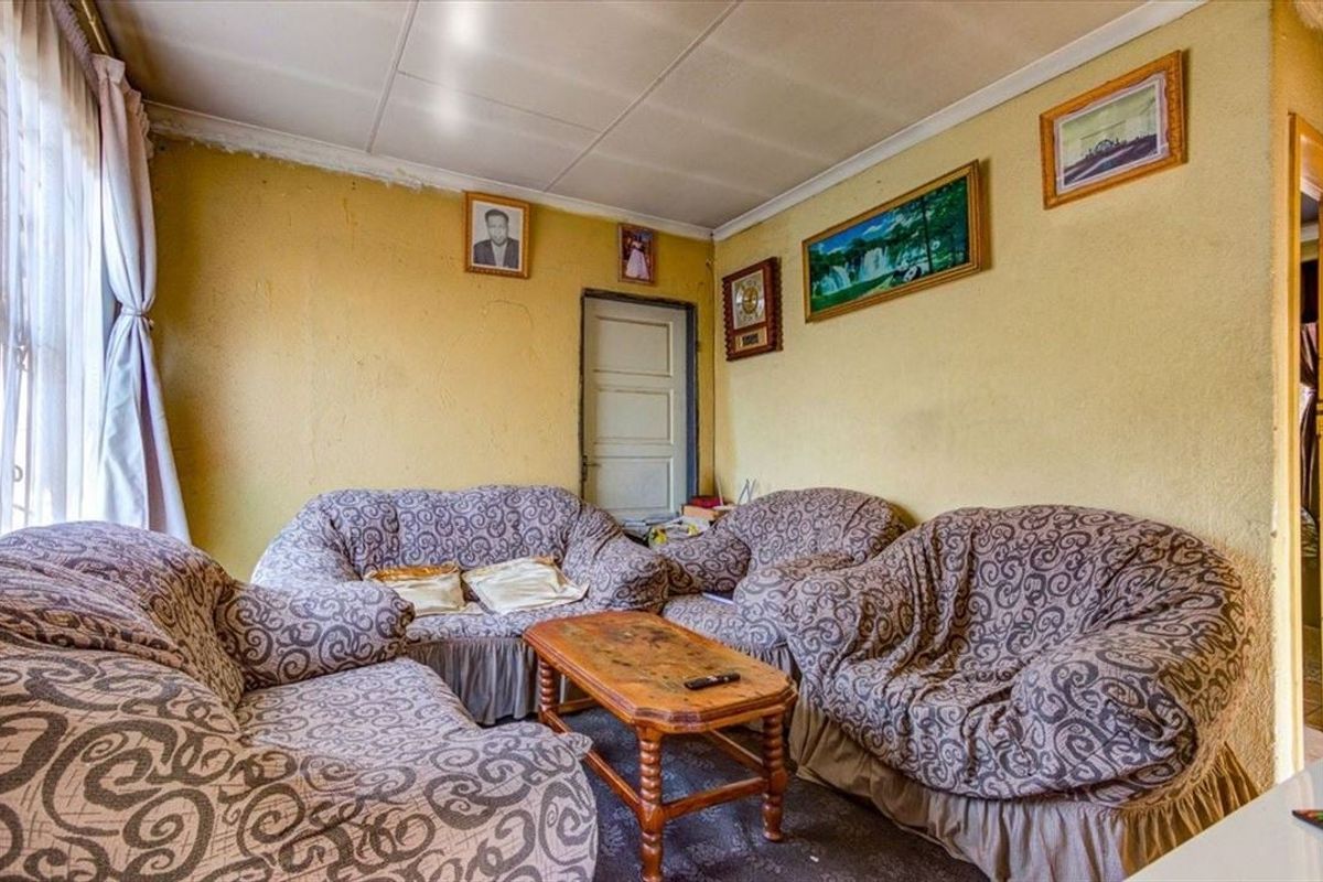A living room space featuring original panelled ceilings and a timber door, currently requiring cosmetic updates and wall repairs to improve the overall finish.