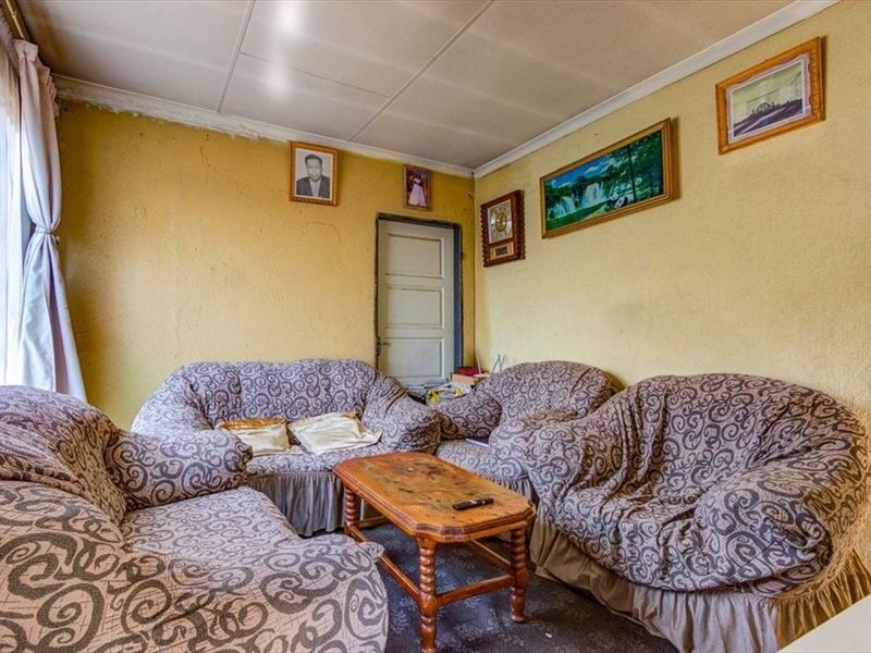 A living room space featuring original panelled ceilings and a timber door, currently requiring cosmetic updates and wall repairs to improve the overall finish.