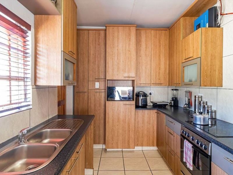 A functional kitchen featuring wood-finish cabinetry, black granite countertops, a double stainless steel sink, and integrated cooking appliances with tiled flooring.