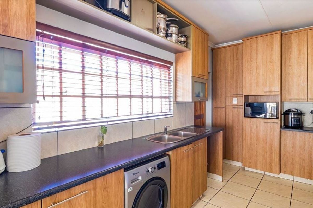 A functional kitchen featuring wood-look cabinetry, dark laminate countertops, a double sink, tiled flooring, and an integrated washing machine.