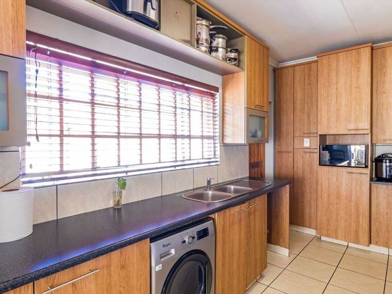 A functional kitchen featuring wood-look cabinetry, dark laminate countertops, a double sink, tiled flooring, and an integrated washing machine.