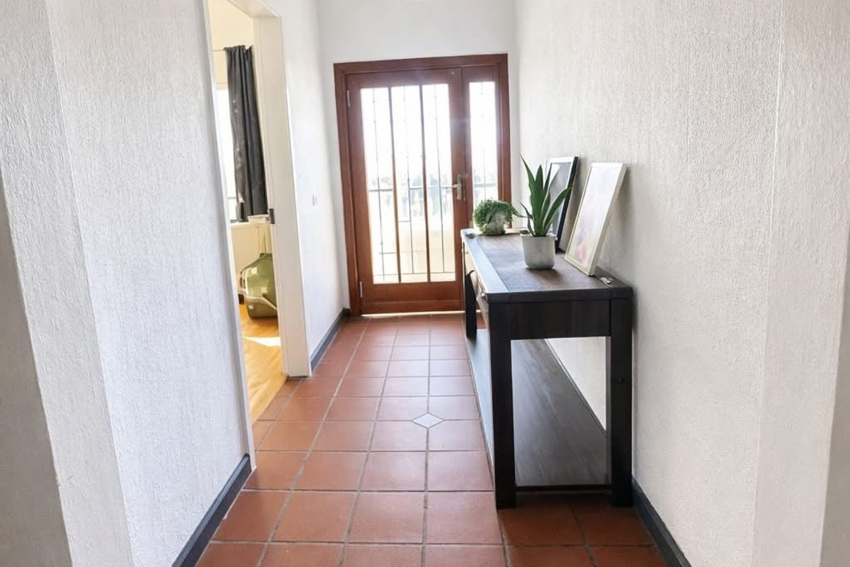 A bright entrance hallway featuring terracotta floor tiles and a timber-framed front door with integrated security gate.