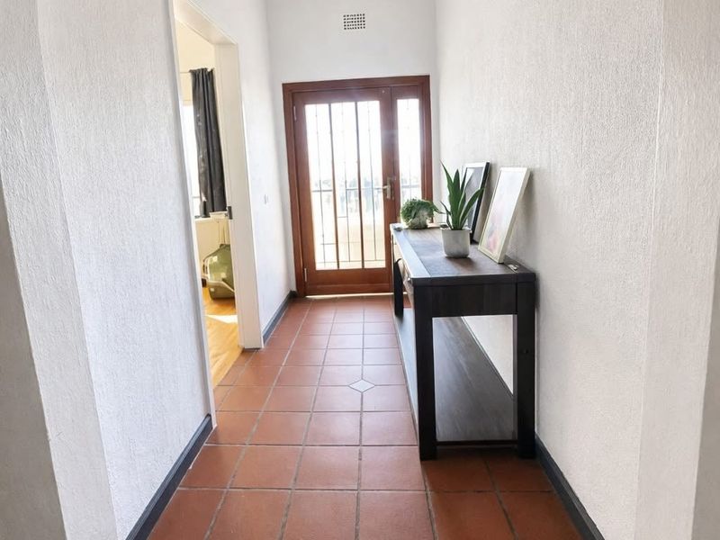 A bright entrance hallway featuring terracotta floor tiles and a timber-framed front door with integrated security gate.