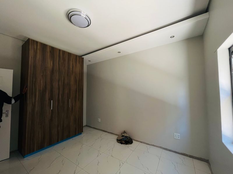 A clean, modern bedroom featuring built-in wood-finish wardrobes, recessed ceiling lighting, and contemporary marble-look tiled flooring.