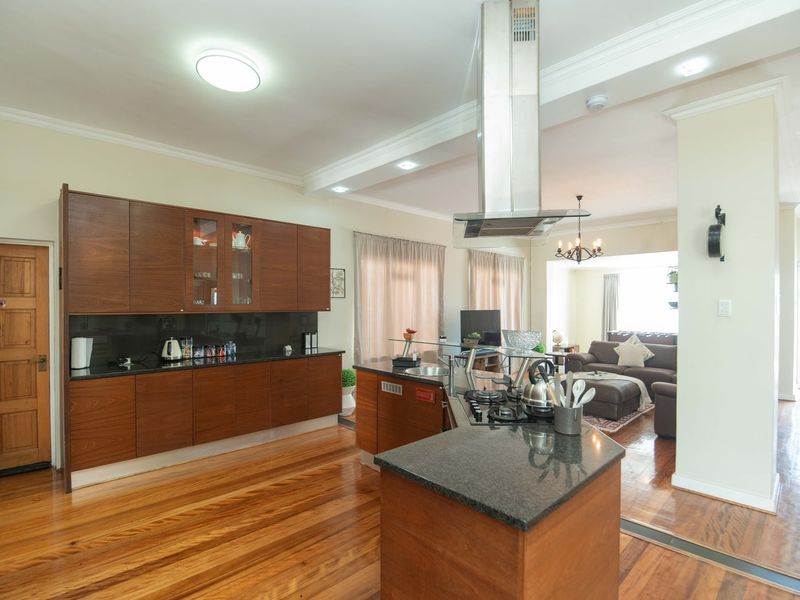 Spacious open-plan kitchen and living area featuring rich wooden cabinetry, granite countertops, a gas hob with extractor, and polished hardwood flooring throughout.