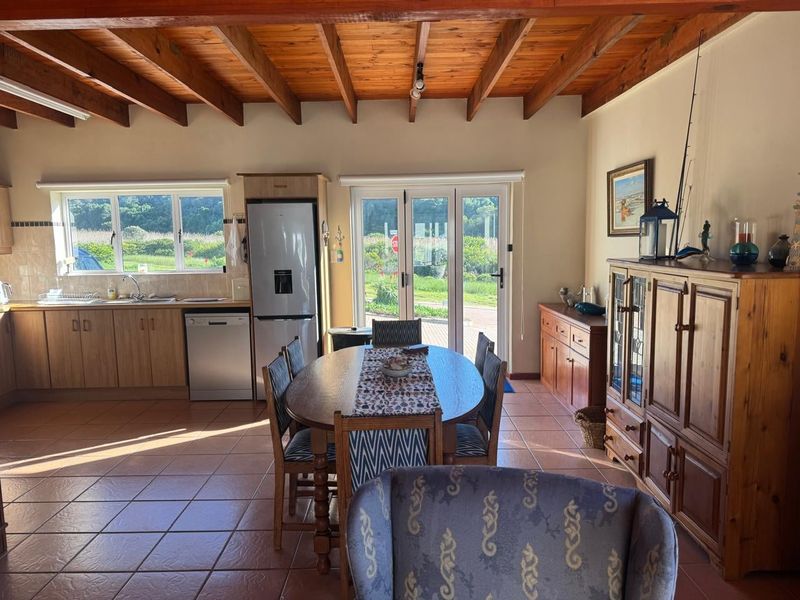 Open-plan living and kitchen area featuring exposed timber beam ceilings, tiled flooring, and direct access to the outdoors through double glass doors.