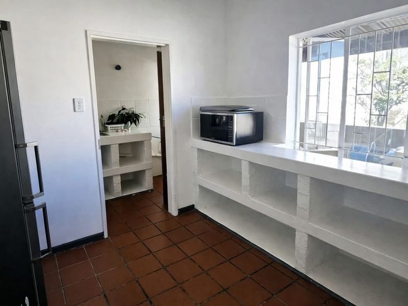A functional scullery area featuring built-in masonry shelving, tiled flooring, and a window with security bars, providing practical storage and prep space.