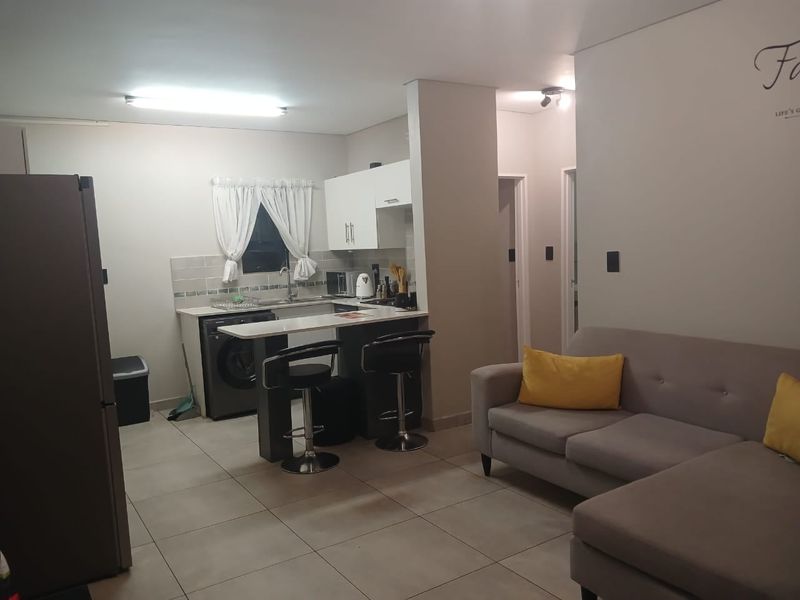 Open-plan living area featuring a functional kitchen with built-in cabinetry, a breakfast bar, and tiled flooring throughout the combined space.