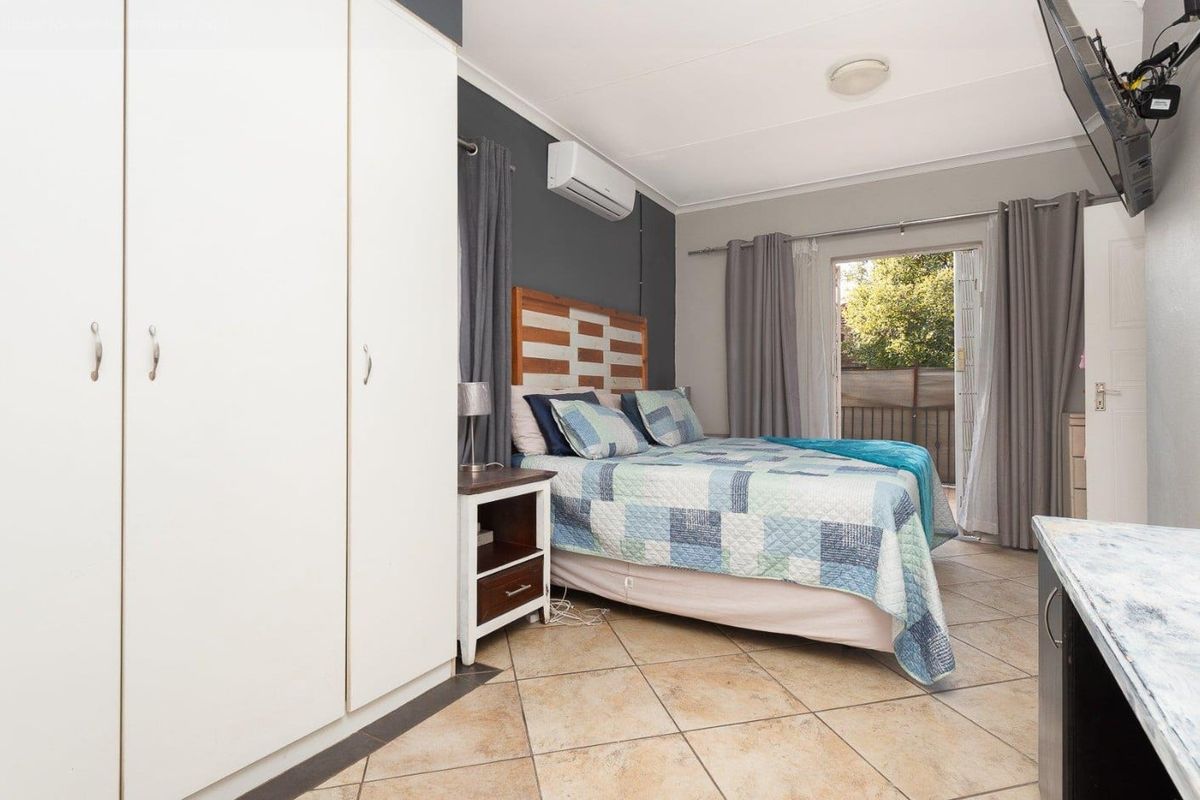 A bedroom featuring built-in wardrobes, tiled flooring, a wall-mounted air conditioning unit, and direct access to an outdoor balcony area.