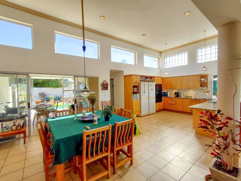 Spacious open-plan living and dining area featuring a functional kitchen with wooden cabinetry, tiled floors, and large windows providing natural light and garden access.