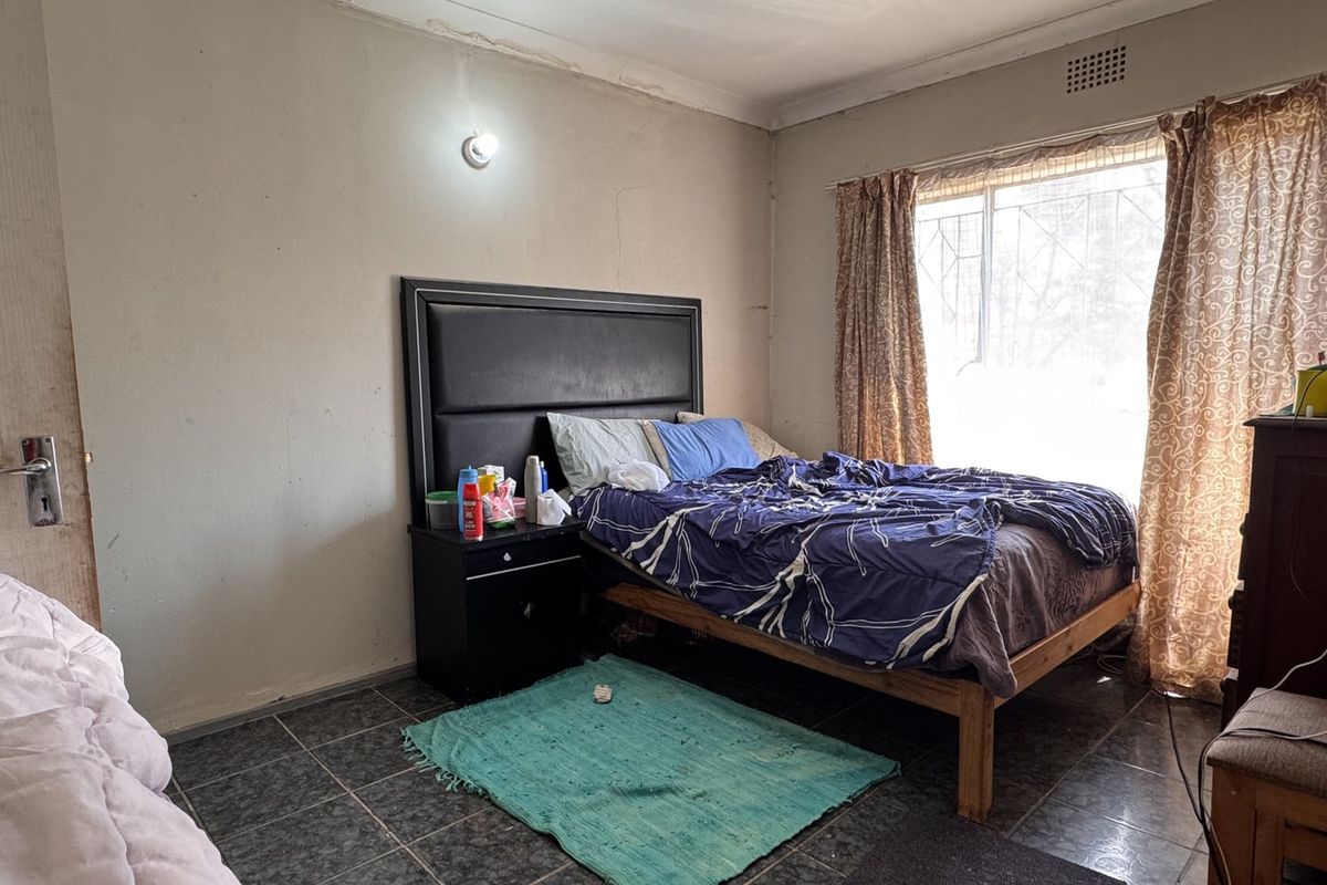 A bedroom featuring tiled flooring and a window with security bars, requiring cosmetic updates to the wall finishes and paintwork.