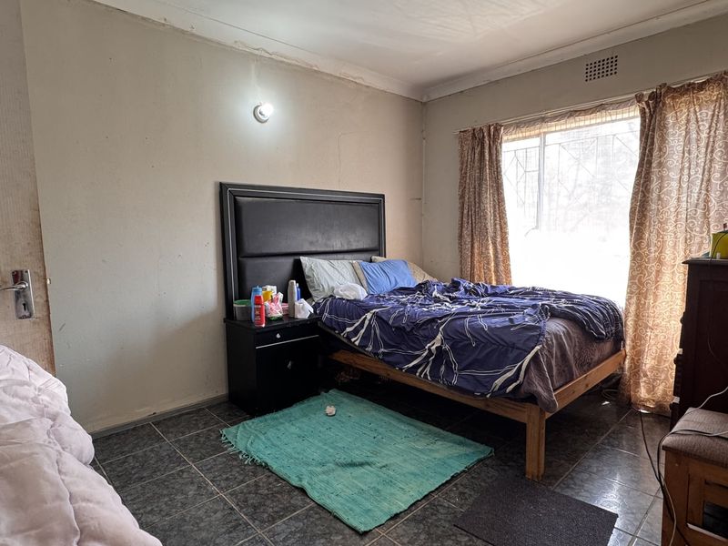 A bedroom featuring tiled flooring and a window with security bars, requiring cosmetic updates to the wall finishes and paintwork.
