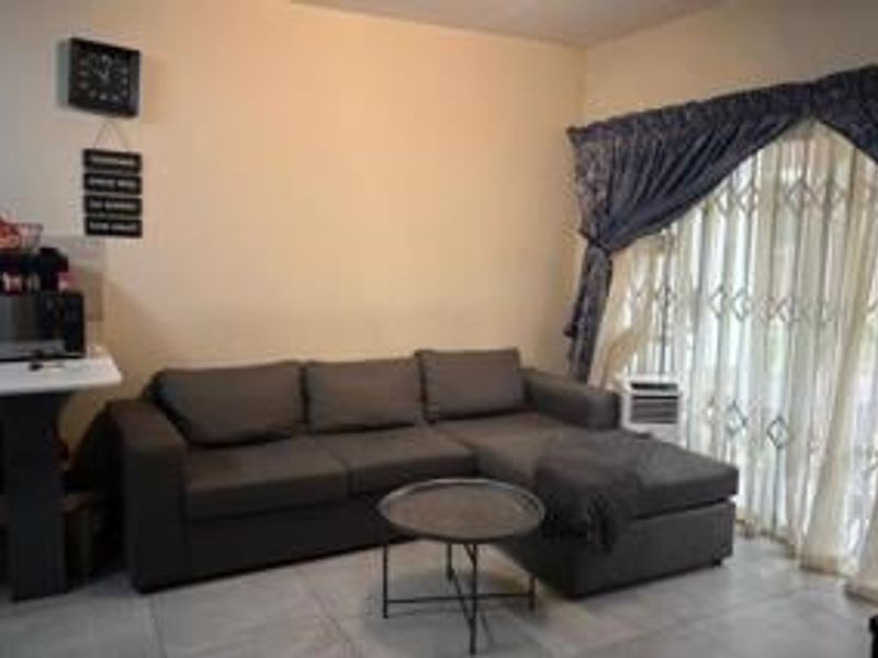 A living room featuring tiled flooring and a sliding glass door with a security gate, providing access to the exterior.