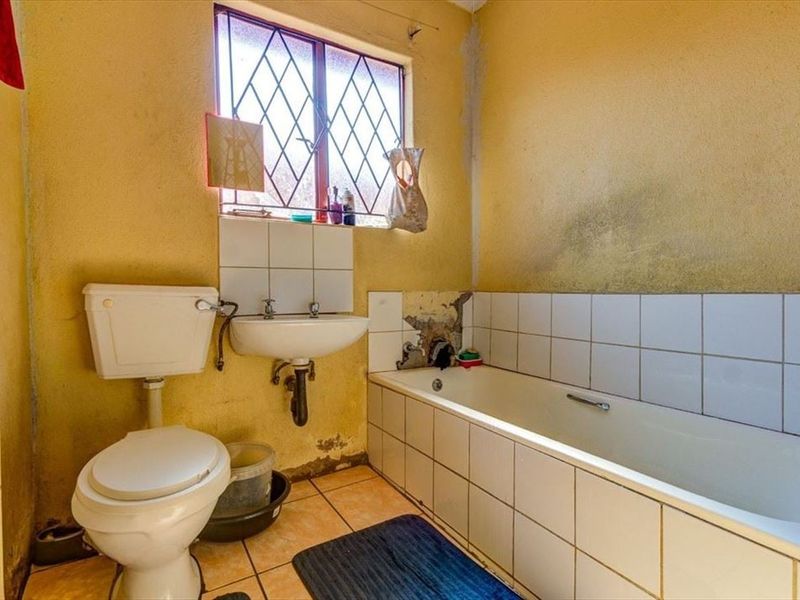 A dated bathroom featuring a standard bathtub, toilet, and washbasin, requiring significant renovation and cosmetic repairs to the wall finishes and tiling.