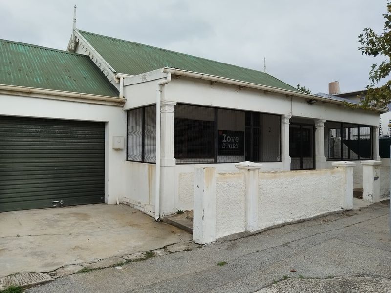 Front elevation of a single-story house featuring a corrugated metal roof, integrated garage with roller door, and a front boundary wall.