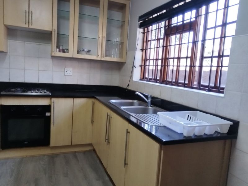 A functional kitchen featuring light wood cabinetry, black granite countertops, a built-in oven, gas hob, and a double sink with a window view.