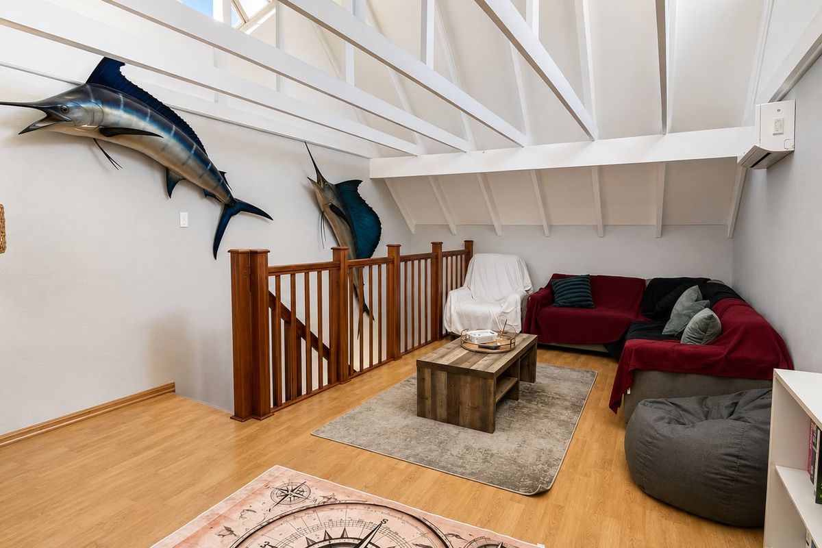 A spacious loft-style living area featuring exposed white timber rafters, high vaulted ceilings, and a wooden staircase with a matching balustrade.
