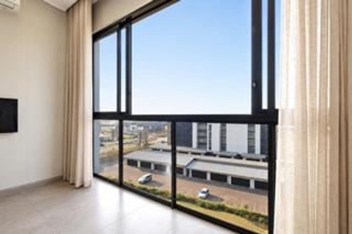 Bright and modern living area featuring expansive floor-to-ceiling windows with neighborhood views, tiled flooring, and a wall-mounted air conditioning unit.