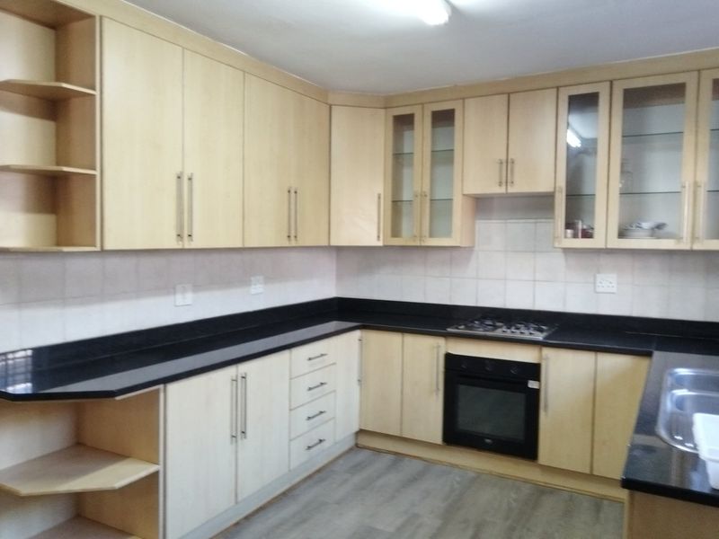 A functional kitchen featuring light wood cabinetry, black granite countertops, a built-in oven, gas hob, and a double sink with tiled backsplash.