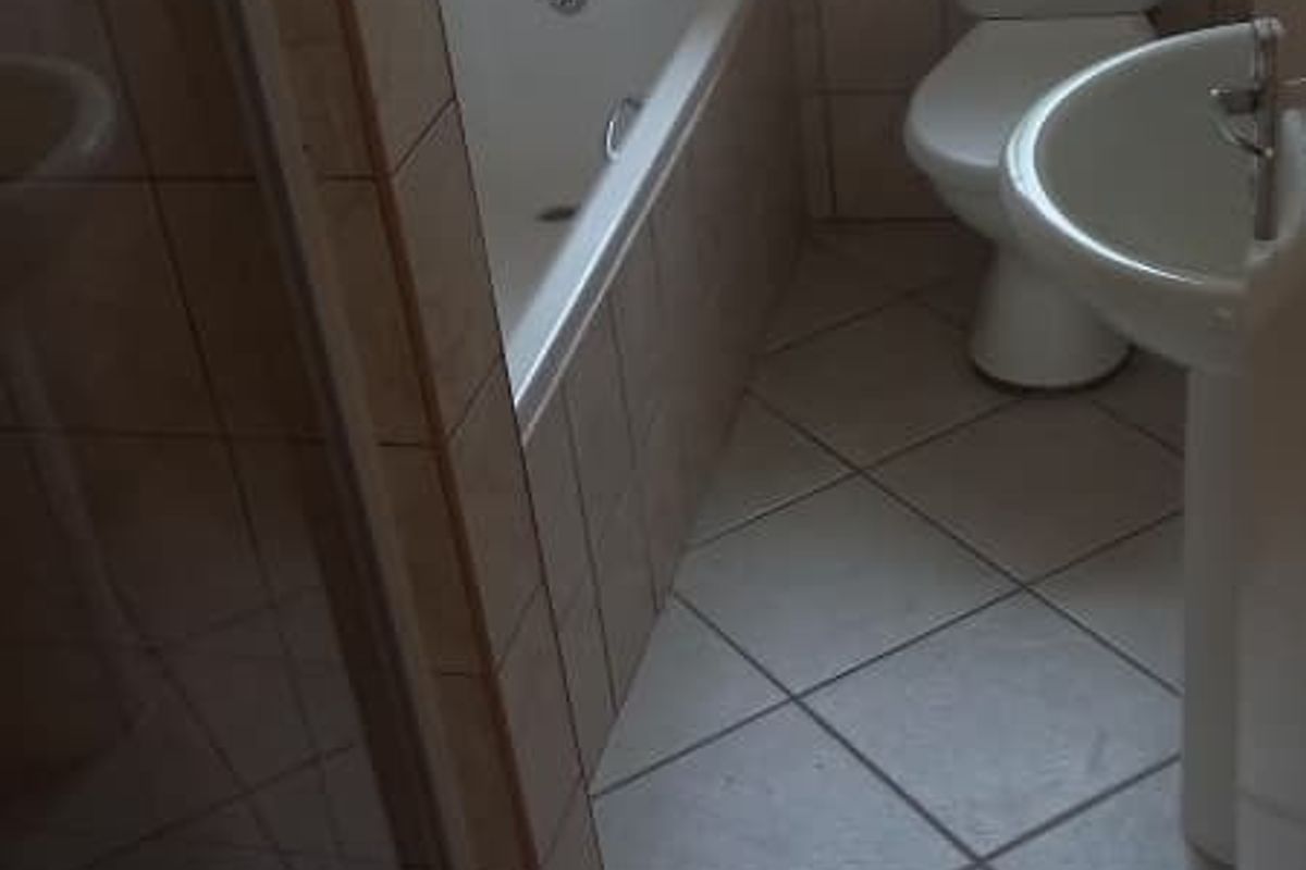 A functional bathroom featuring a bathtub, separate shower enclosure, pedestal basin, and toilet, finished with neutral floor and wall tiling.
