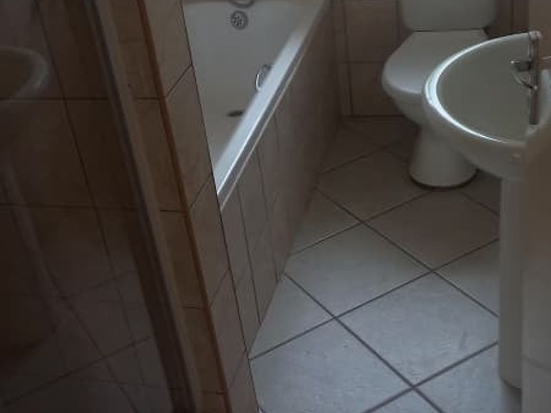 A functional bathroom featuring a bathtub, separate shower enclosure, pedestal basin, and toilet, finished with neutral floor and wall tiling.