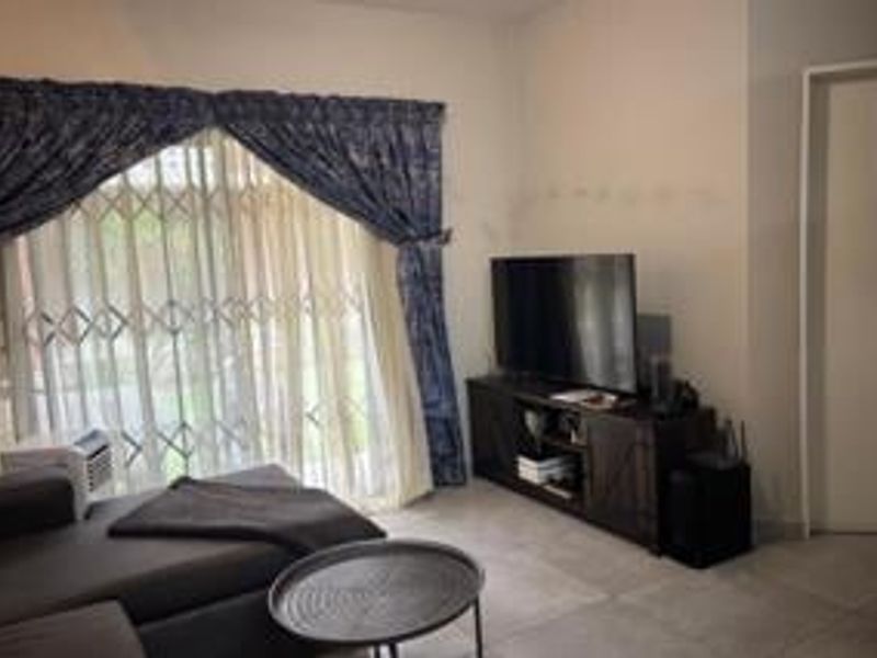 A living room featuring tiled flooring and a sliding door with a security gate, providing access to the exterior.