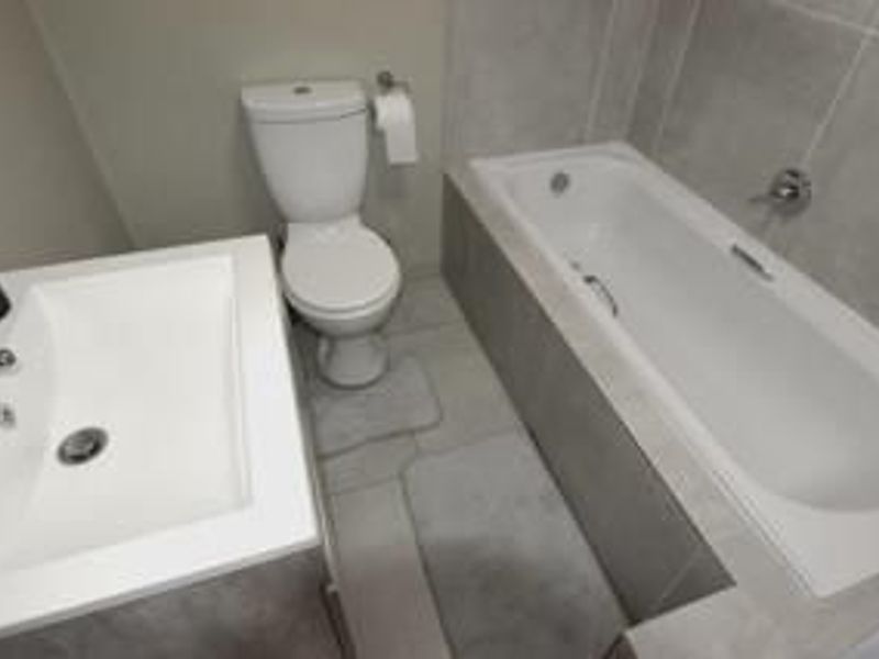A clean and modern bathroom featuring a built-in bathtub, a white ceramic toilet, and a vanity basin with neutral grey wall and floor tiling.