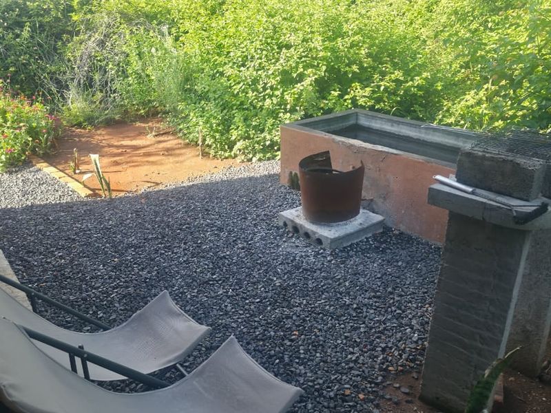 Outdoor patio area featuring a built-in braai, concrete trough, and gravel landscaping, set against a natural bushveld backdrop.