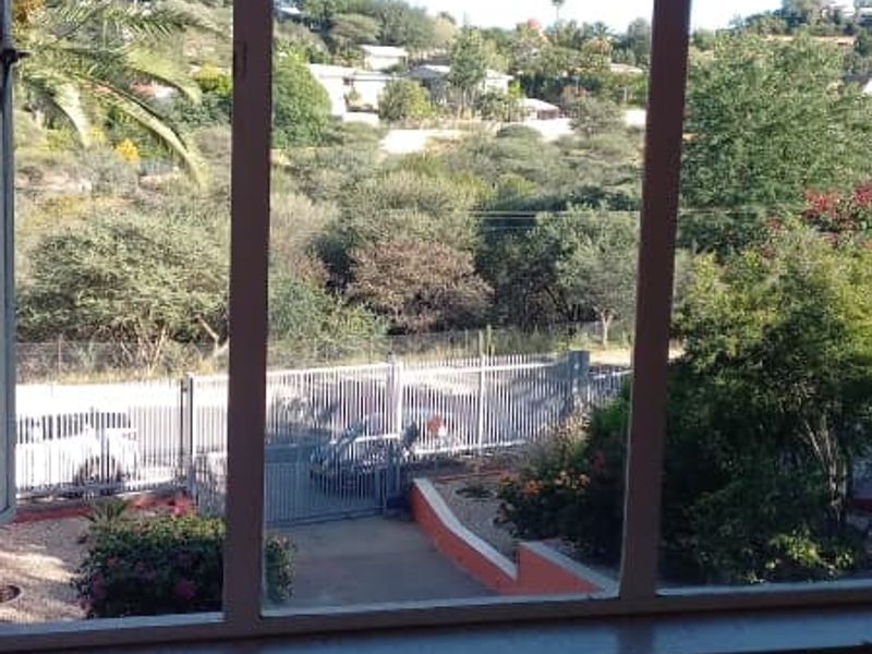 A view looking out through metal-framed windows towards a residential street and hillside landscape.