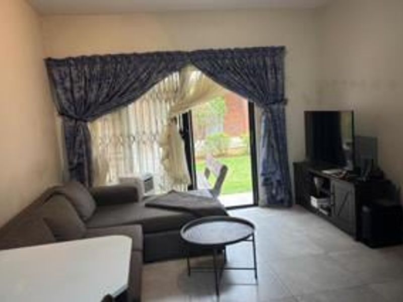 A living room featuring tiled flooring and a sliding glass door with a security gate, providing access to the outdoor area.