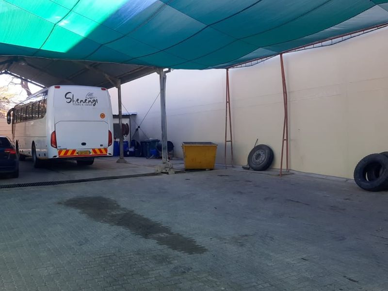 A large covered outdoor parking or utility area featuring a shade cloth canopy, paved flooring, and integrated drainage, suitable for vehicle storage.