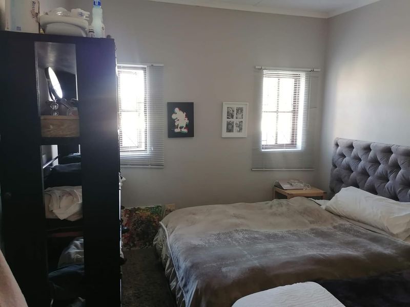 A bedroom featuring two windows with venetian blinds and a tufted upholstered headboard.