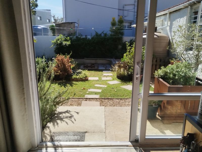 View from a sliding glass door looking out onto a rear garden with a concrete patio, stepping stone path, and water storage tank.