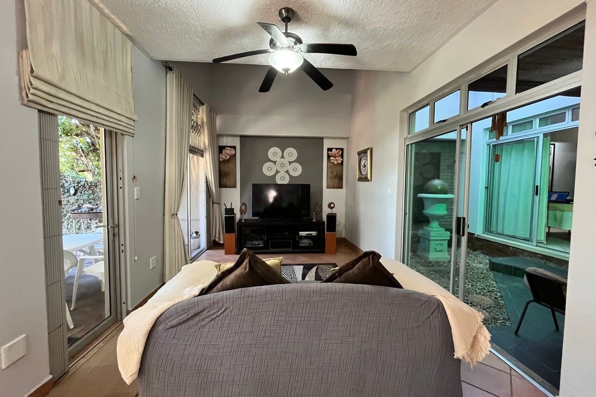 Spacious living room featuring high ceilings, a central ceiling fan, and large sliding glass doors providing access to outdoor patio and courtyard areas.