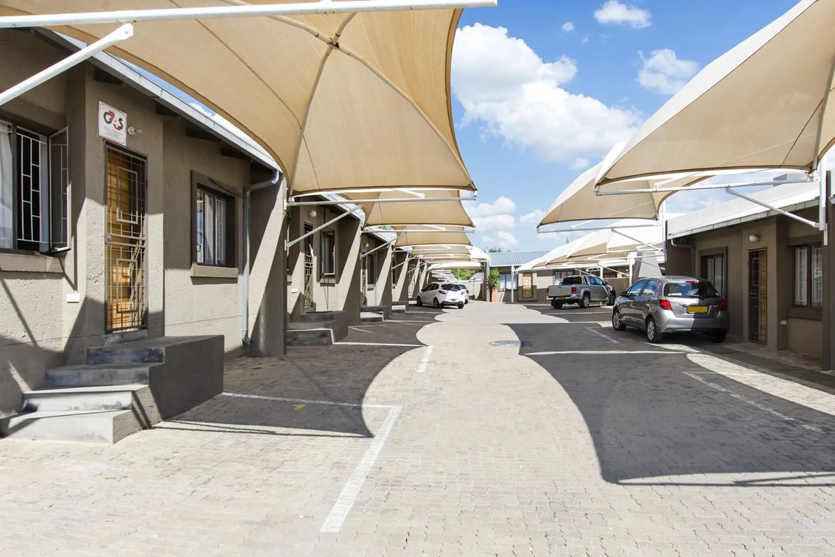 Exterior view of a townhouse complex featuring a paved driveway with multiple shade sail carports and secure unit entrances.